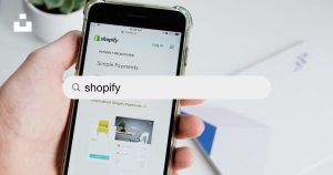 Illustration of a person selecting the best Shopify agency for their business growth. Hand holding phone looking up shopify on the web starting at a screen of shopify.