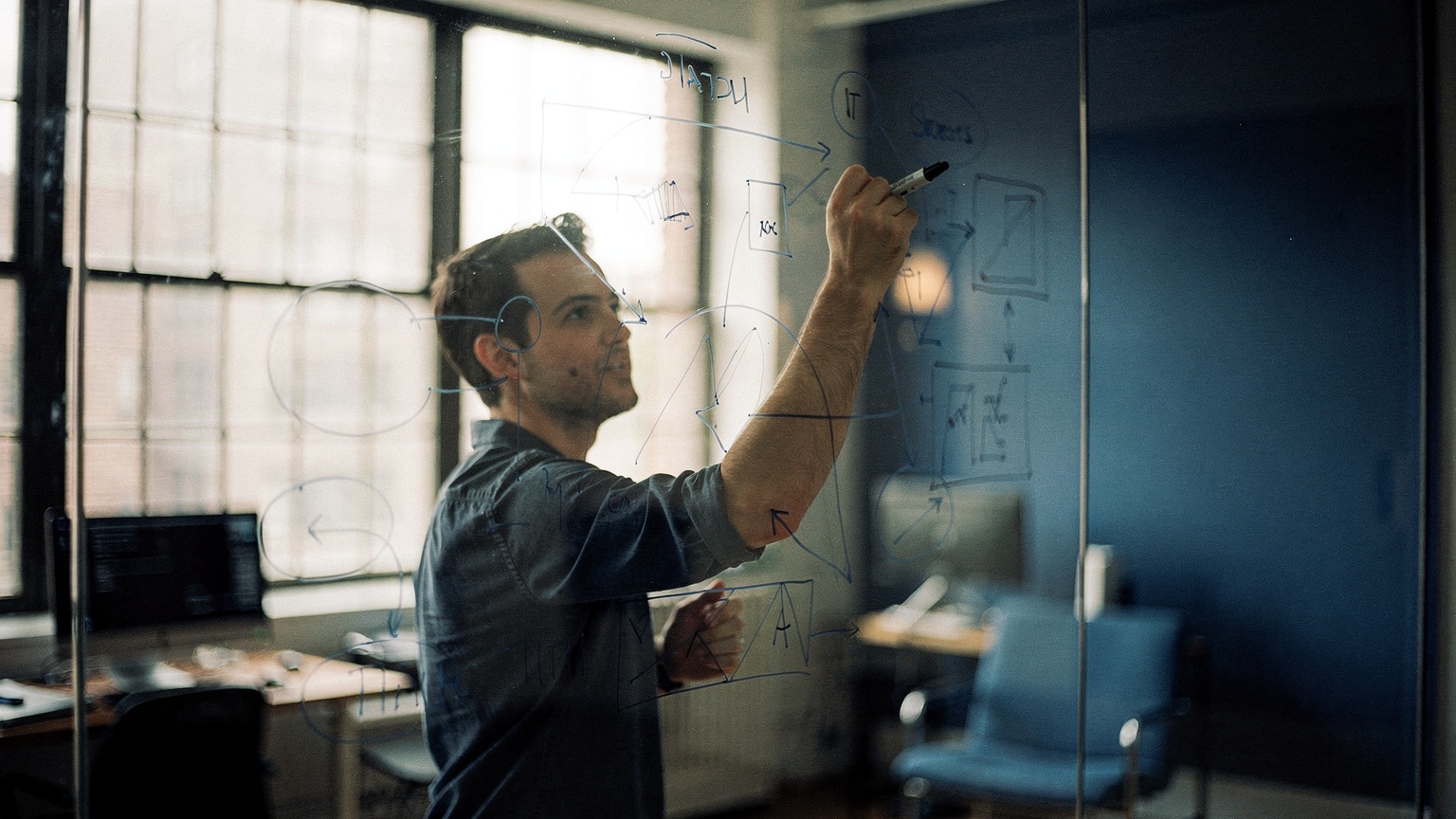 An integration architect mapping Magento ERP data flows on a glass wall in a Brooklyn studio