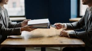 A calm handover of access notes and documents between two professionals in a Brooklyn office