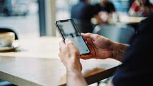 A shopper completing a Magento purchase on a smartphone in a bright cafe