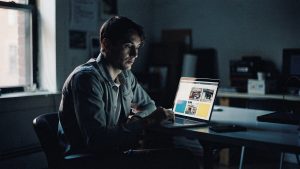An operations lead reviewing several regional Magento storefronts on a laptop in a Brooklyn studio