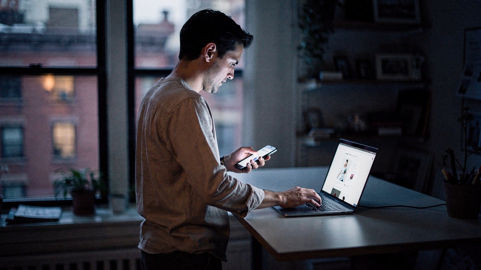 Frontend developer comparing a fast-loading Magento store on a smartphone and laptop in a Brooklyn studio