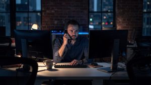 eCommerce operations director alone in a dark Brooklyn office at night on a landline phone beside powered-off monitors