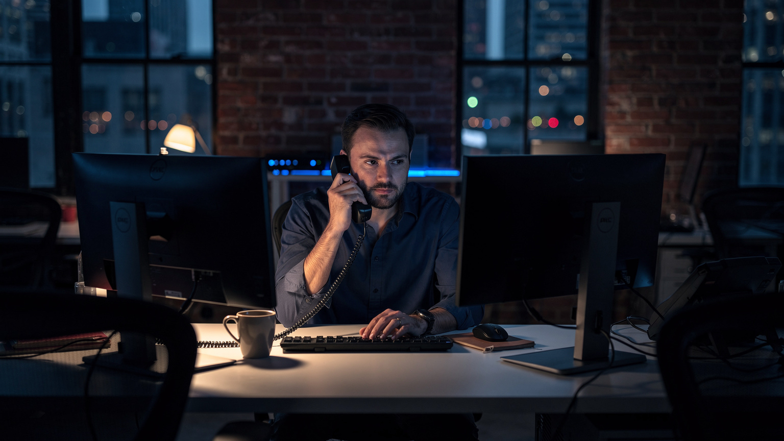 eCommerce operations director alone in a dark Brooklyn office at night on a landline phone beside powered-off monitors